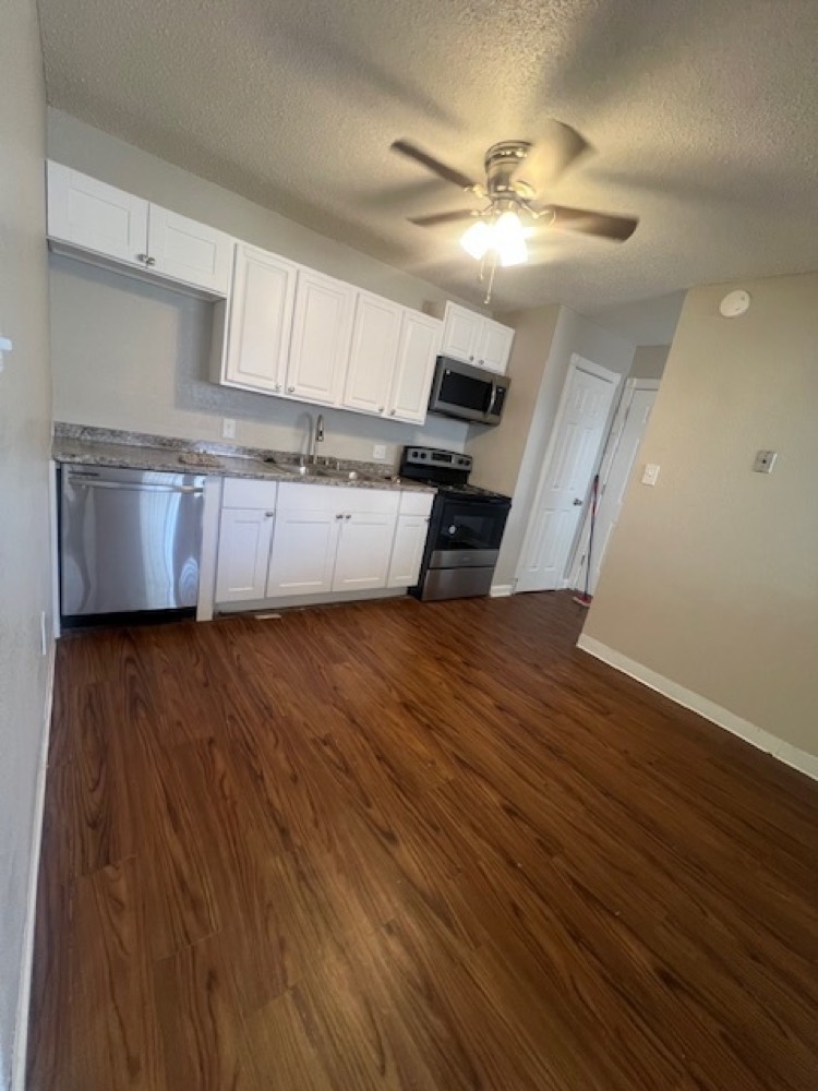 A renovated one bedroom kitchen with white cabinets, stainless steel appliances, and dark wood-look flooring