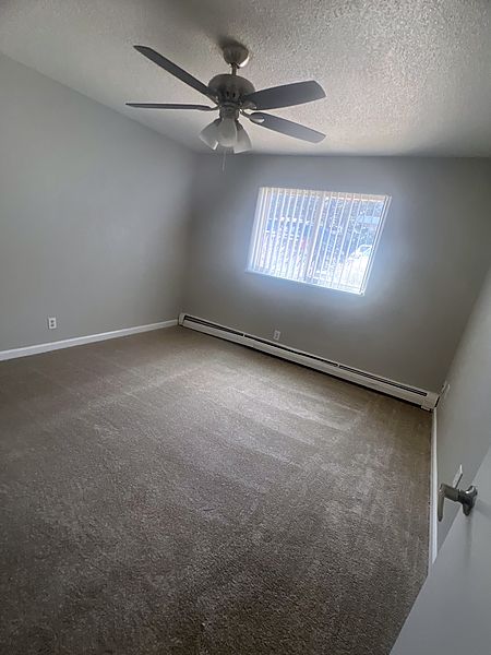 Carpeted bedroom with a ceiling fan and a window with vertical blinds