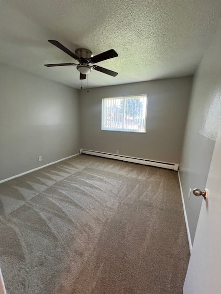 Carpeted bedroom with ceiling fan and baseboard heating