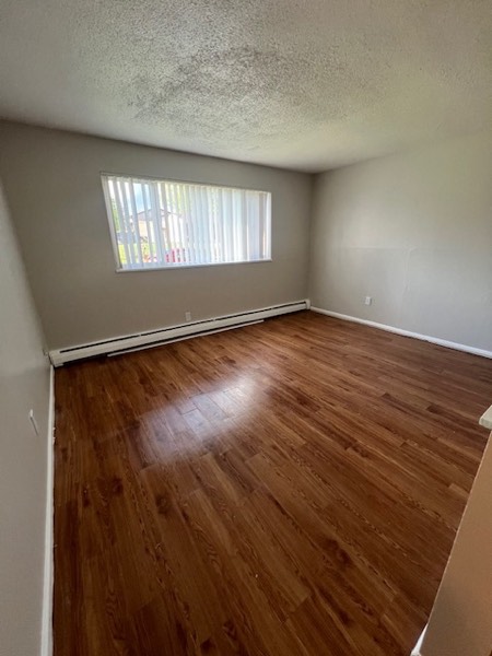 Bedroom with warm wood flooring and a wide window with blinds