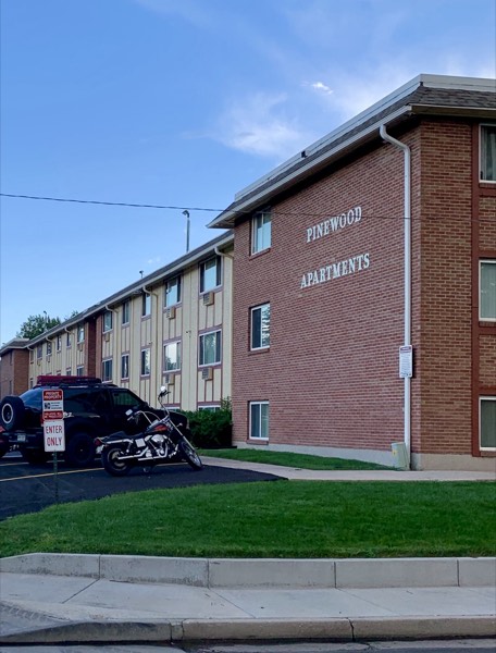 Corner view of the brick building with Pinewood Apartments lettering above the parking area