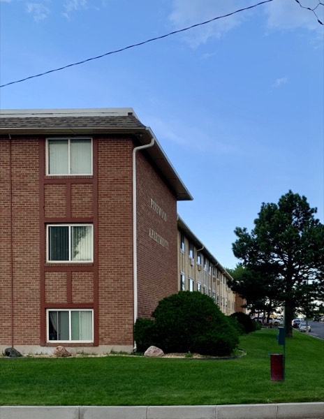 Brick corner of Pinewood Apartments with the building extending back past a tall pine