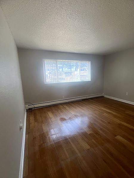 Living room with polished hardwood floors and a wide window above the baseboard heater